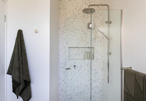 renovated bathroom shower with terrazzo feature tiles, a built-in shower niche and multiple towel rails