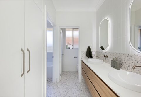 renovated 3-way bathroom using terrazzo floor tiles, floating double vanity in wood finish, brushed nickel tapware, oval LED mirrors