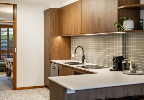 renovated kitchen, mid-century style with engineered stone benchtops, small green square tiles on splashback, cabinetry on Florentine walnut finish and terrazzo floor tiles.