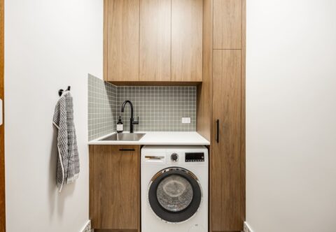 renovated laundry, mid-century style with small green square tiles on splashback, cabinetry on Florentine walnut finish and washer dryer combo