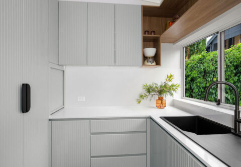 renovated compact kitchen with mid-century style, bespoke joinery with grooved profiles in green-grey paired with walnut details