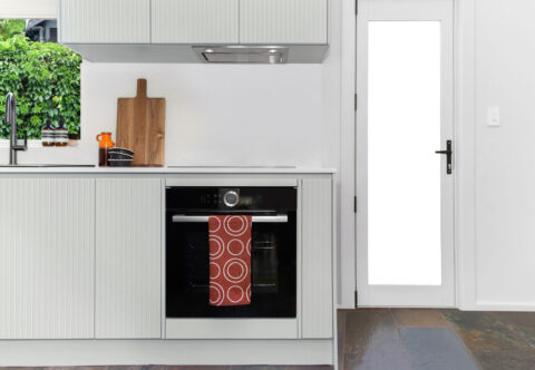 renovated compact kitchen with mid-century style, bespoke joinery, glass splashback and black appliances