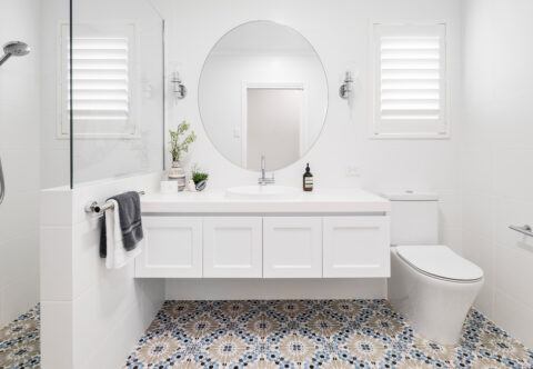 renovated bathroom, Hamptons classic style with walk-in shower, grab rails, decorative floor tiles, floating vanity with shaker profiles and large round mirror.