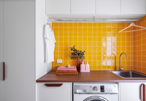 renovated laundry, mid-century style with yellow square tiles and custom joinery, designed wood top and handles, a hanging rail, washer and sink