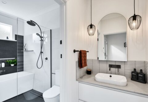 renovated bathroom with stone top and splashback, curved mirror, black industrial ceiling lights, open shower and back-to wall bathtub