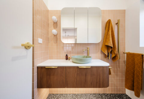 renovated bathroom, retro style with gorgeous pink tiles on walls and dark grey terrazzo tiles on the floor, floating vanity in, brushed brass tapware and curved mirror cabinets