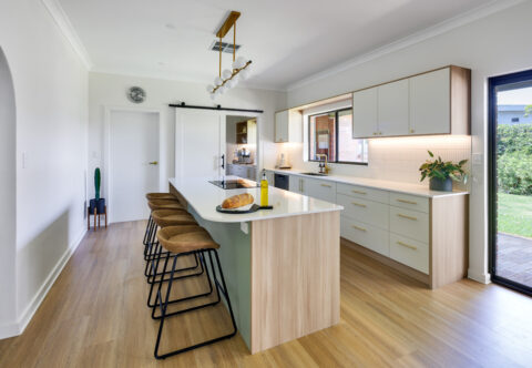renovated kitchen, retro style with breakfast bar on kitchen island light pendant, bespoke joinery in green, white and wood finishes paired with brushed nickel handles
