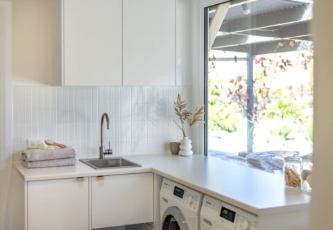renovated laundry, small and functional, with washer and dryer, sink, L-shape benchtop and area for the cat's litter box