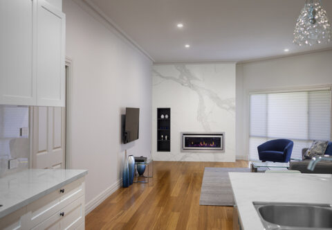 renovated living room with featured fireplace, porcelain cladding wall with matching grain, woodgrain open shelving, built-in gas fireplace