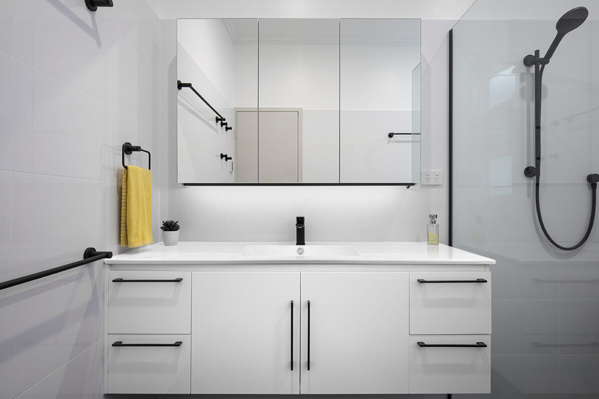 renovated bathroom, with large vanity, mirror cabinets, using black fixtures and fittings and white cabinetry.
