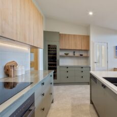 renovated kitchen, and living room of 1920s California Bungalow, beautiful green cabinetry paired with Tasmanian oak, an integrated wine fridge, open shelves and pretty of storage.