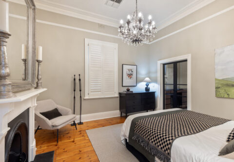 renovated master bedroom, cantered king bed with nightstands and wall sconce lights, traditional chandelier hanging from the ceiling, original fireplace