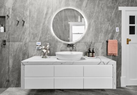 renovated bathroom, luxurious with large format porcelain tiles in grey and white tones, freestanding vanity, marble stone benchtop and an illuminated mirror.