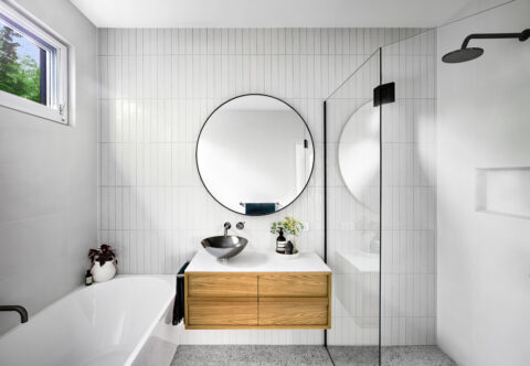 renovated bathroom, Scandinavian style with wall-mounted vanity in, stainless-steel basin, round mirror, bathtub and shower, sophisticated floor-to-ceiling tiles