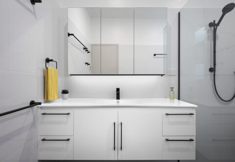 renovated bathroom, with large vanity, mirror cabinets, using black fixtures and fittings and white cabinetry.