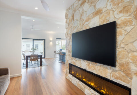 renovated living area with featured stone wall and with modern fireplace, TV and solid timber flooring