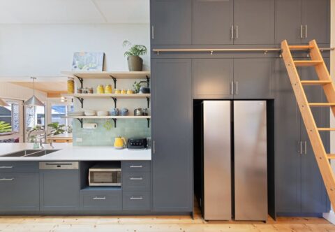 renovated kitchen, Zellige tiled splashback in pale green, freshly polished solid wood floors, bespoke joinery in deep blue paired wooden floating shelves with a custom library ladder
