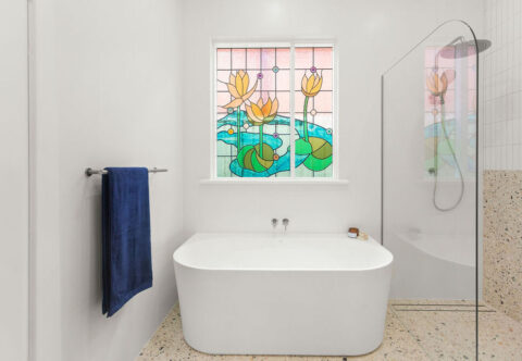 Renovated bathroom with traditional tinted window, free standing bathtub, walk-in shower and terrazzo looking tiles.