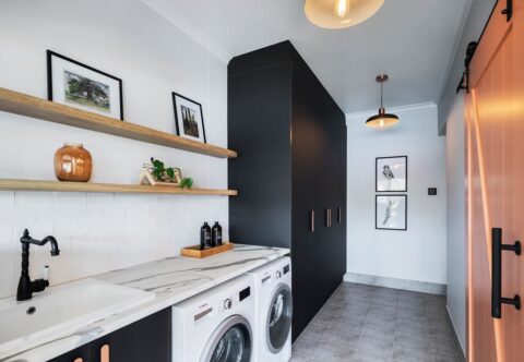 renovated laundry, modern style with matte black cabinetry, with laminated benchtops, tangerine barn door and open shelves.