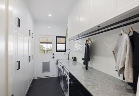 renovated laundry in black and white tones, set of hanging rails, engineered stone benchtop and herringbone wall tiles