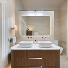 Renovated bathroom in Glenelg, with a mid-century style, a double basin vanity, shaving cabinets, and layered lighting.