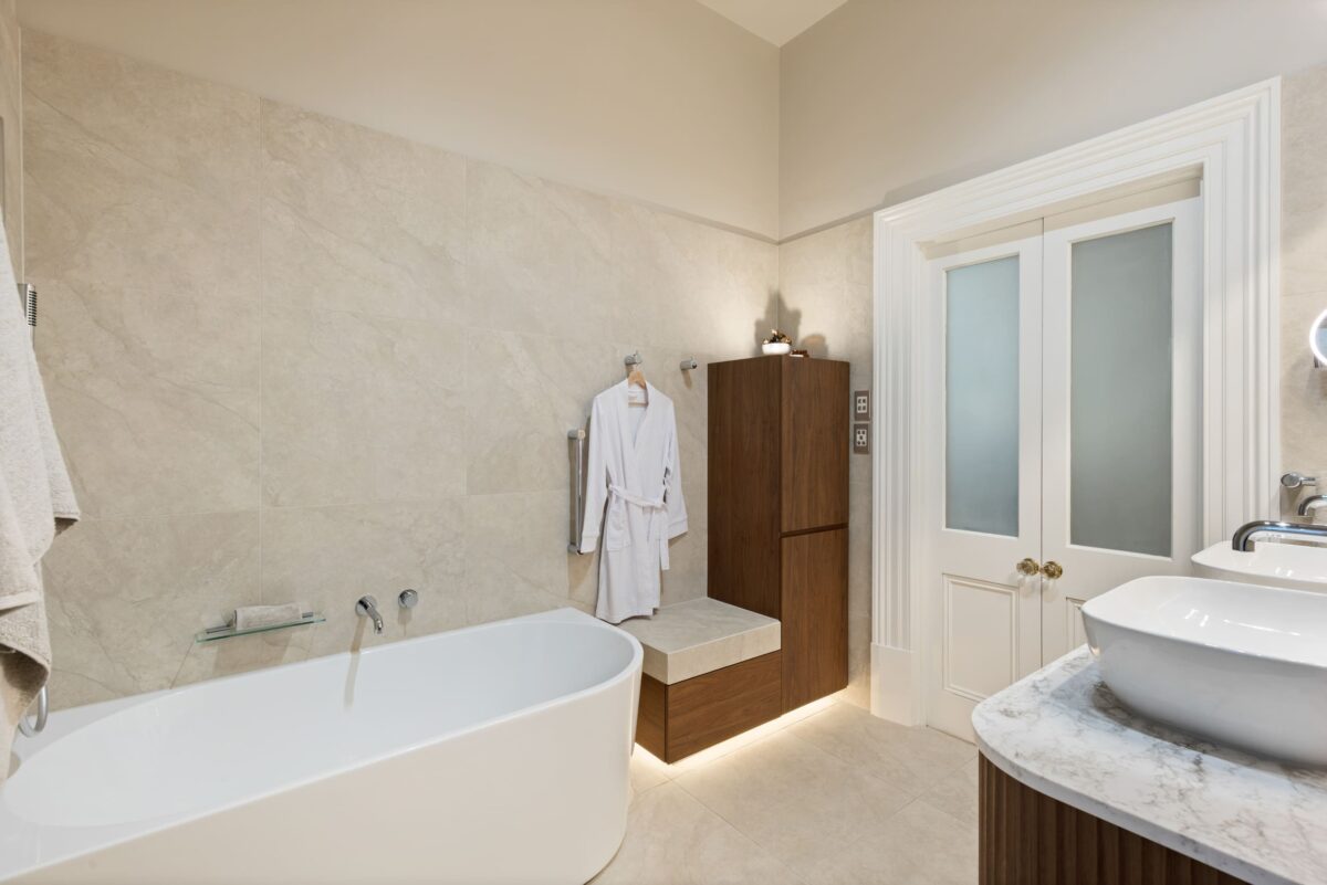 Renovated bathroom in Glenelg, with a back-to-corner bathtub, heated towel rails, a bench seat and plenty of storage, including a laundry hamper.