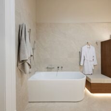 Renovated bathroom in Glenelg, with a back-to-corner bathtub, heated towel rails, a bench seat and plenty of storage, including a laundry hamper.