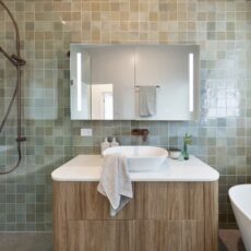 Renovated bathroom in Japandi style, soft sage green tiles, white and timber vanity paired with brushed bronze tapware.