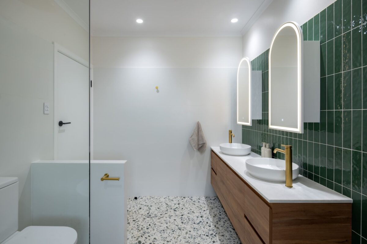 Renovated family bathroom with modern style, featuring green tiles, wall-hung vanity, twin mirror cabinets and brushed brass accessories.