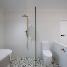 Renovated bathroom with terrazzo-look floor tiles, brushed brass tapware, and a walk-in shower.
