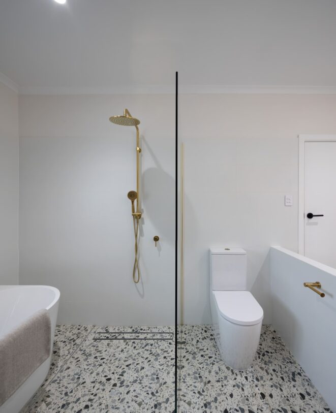 Renovated bathroom with terrazzo-look floor tiles, brushed brass tapware, and a walk-in shower.