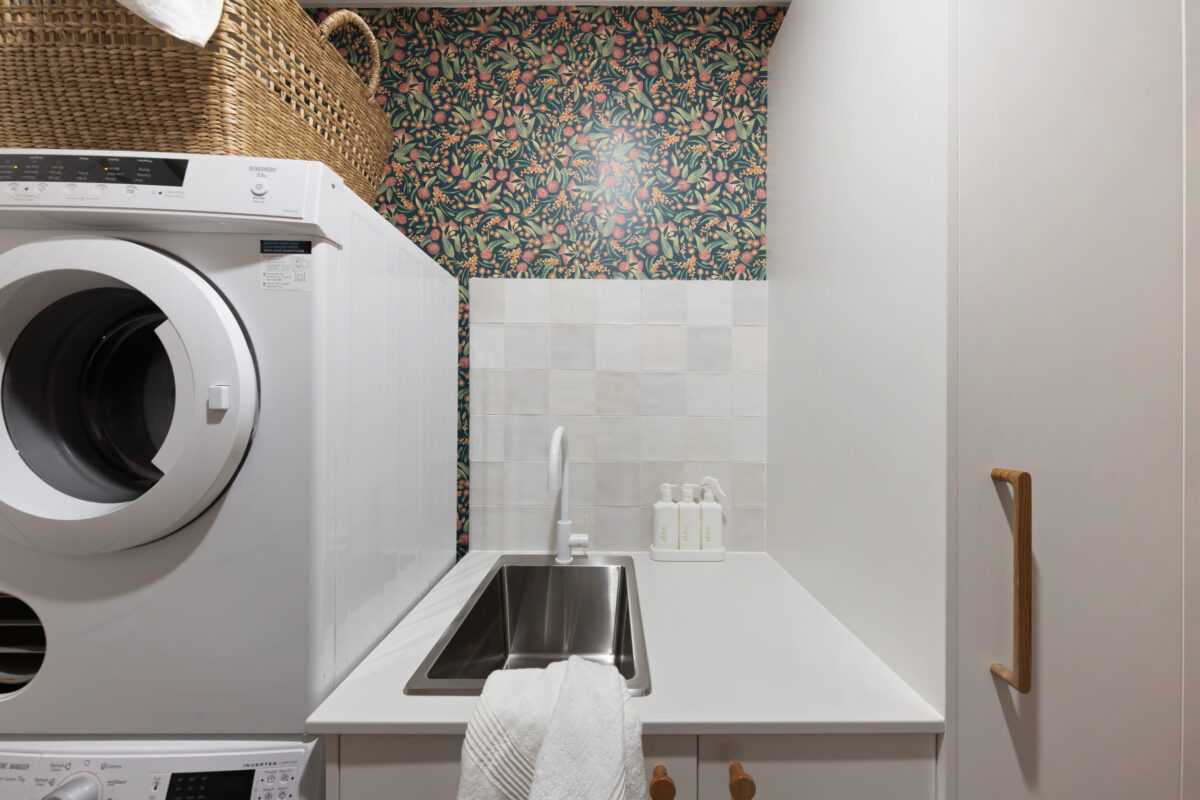 Renovated laundry with floral wallpaper and white cabinetry