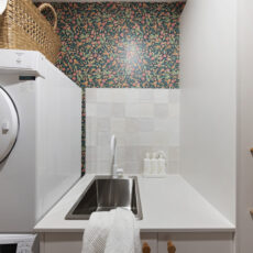Renovated laundry with floral wallpaper and white cabinetry