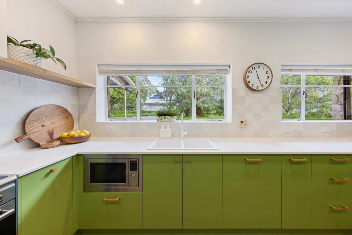 Renovated kitchen in Blackwood with retro-inspired style, vibrant green cabinetry, solid timber shelves and white benchtops.