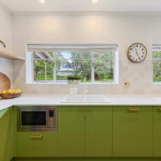 Renovated kitchen in Blackwood with retro-inspired style, vibrant green cabinetry, solid timber shelves and white benchtops.